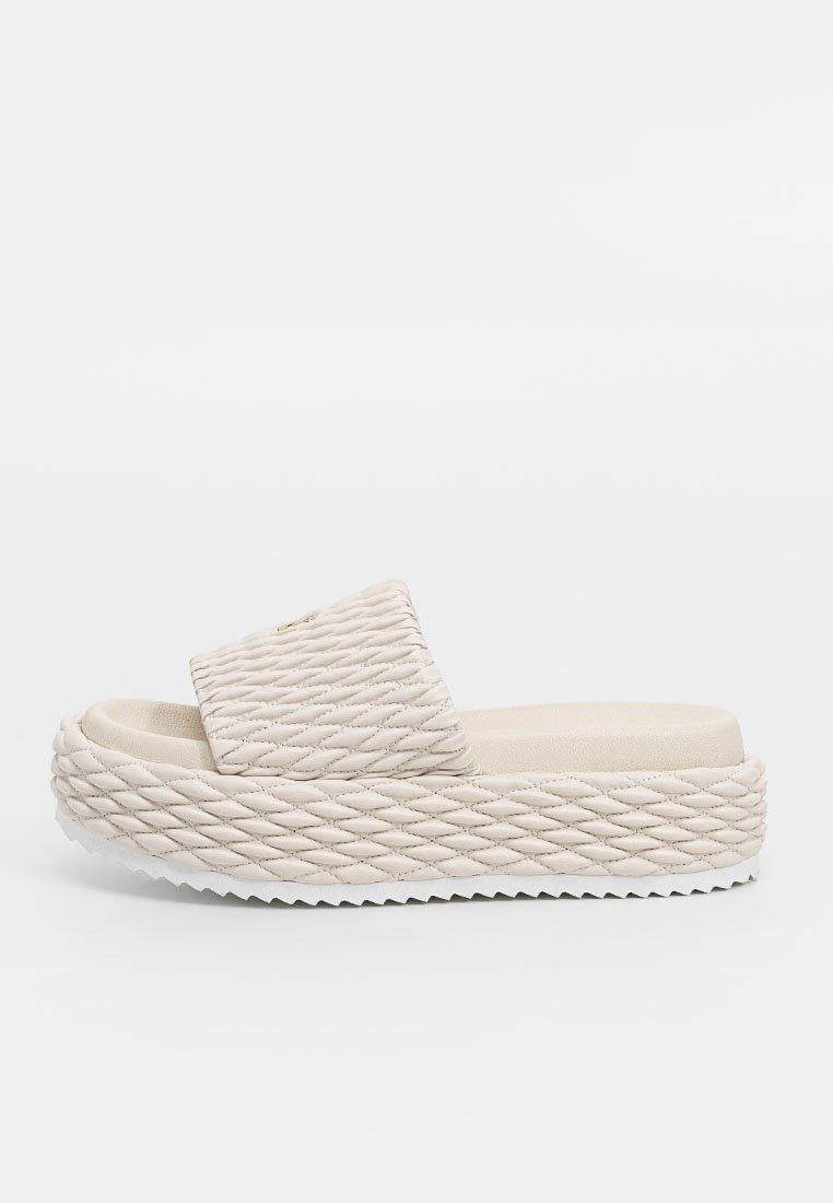 Beżowe sandały na platformie z plecionym wzorem, z szerokim górnym paskiem i teksturowaną gumową podeszwą. Prosta, nowoczesna estetyka.