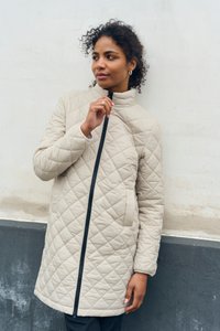 Beige gesteppter Mantel mit hohem Kragen, ausgestattet mit einem durchgehenden schwarzen Reißverschluss und dezenten Rautenmustern auf dem Stoff.