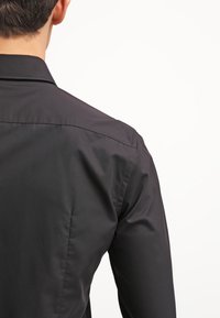 Zwart shirt met lange mouwen en een gladde stoftextuur; heeft een klassieke kraag en nette stiksels langs de schouders en rug.