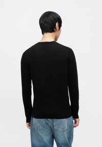 Juodas megztinis ilgomis rankovėmis su apvalia iškirpte, pasižymintis lygiu paviršiumi, aptempiančia forma ir ribbingu kišnelių bei apačios dalyje.