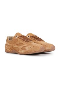Chaussures de sport en daim beige avec lacets marron, surface texturée et découpes latérales. Elles présentent une semelle en caoutchouc et un design à bout arrondi.