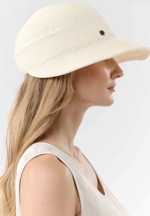 Woman with long blonde hair wearing a sleeveless beige top and a cream woven sun hat with a small black emblem on the side.