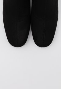 Botines de ante negros con puntera afinada, textura suave, detalle de costura mínima y un diseño elegante. Suelas planas, estilo versátil.