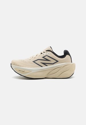 Beige New Balance løbesko med tyk polstret sål, sort indvendigt foer og stort sort "N" logo på siden.