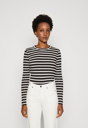 Top a maniche lunghe bianco e nero a righe con scollatura rotonda, tessuto texturizzato, abbinato a jeans bianchi a vita alta.