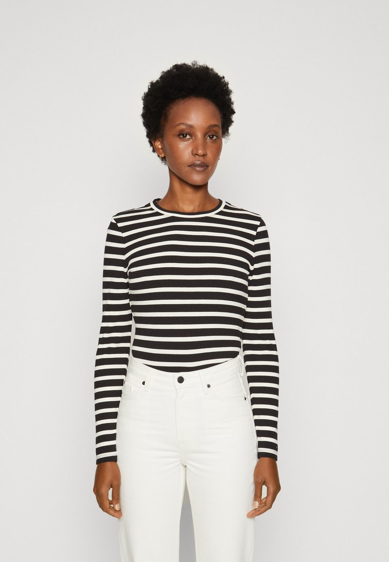 Top a maniche lunghe bianco e nero a righe con scollatura rotonda, tessuto texturizzato, abbinato a jeans bianchi a vita alta.
