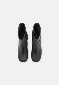 Paire de bottines en cuir noir avec fermetures éclair latérales, bouts carrés arrondis et doublures intérieures visibles, vues de dessus sur fond blanc.