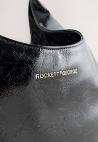 Zwarte nep leren tas met een gestructureerd oppervlak, voorzien van een gouden "ROCKETT st GEORGE" logo. Gebogen vorm, open bovenkant ontwerp.