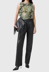 Femme portant un top sans manches floral vert, un pantalon en cuir noir, des bottes à talons aiguilles noires, tenant un sac en cuir frangé noir.