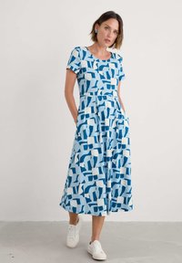 Blue and white patterned dress with short sleeves, round neck, pockets, and flowing silhouette. Textured fabric featuring abstract shapes.