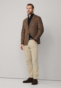 Blazer marron à carreaux, chemise navy, pantalon beige, bottes chelsea marron ; coupe ajustée avec revers crantés et poches à rabat. Tissu et motif subtils.