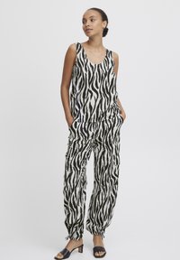 Jumpsuit sa zebrinim uzorkom u crno-bijeloj kombinaciji, bez rukava, s širokim hlačama i bočnim džepovima. Lagana tkanina i manžetne s vezicom.