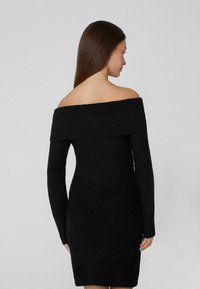 Černé žebrované šaty bez ramínek s dlouhými rukávy, přiléhavého střihu a texturovaného materiálu, s rovně střiženým výstřihem a minimálními detaily.