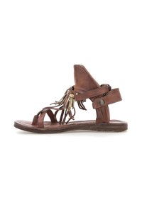 Brune læder flad sandal med ankelstrop, åben tå, frynser med kvaster og metalring dekorationer på en hvid baggrund.