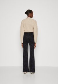 Pullover bej tricotat cu guler rotund, asortat cu pantaloni evazați navy cu model. Contrastul de texturi între tricotul moale și țesătura netedă.