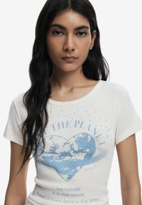 Witte katoenen t-shirt met een lichtblauw hartontwerp met een planetenmotief, blauwe tekst en verspreide blauwe accenten rond de halslijn.