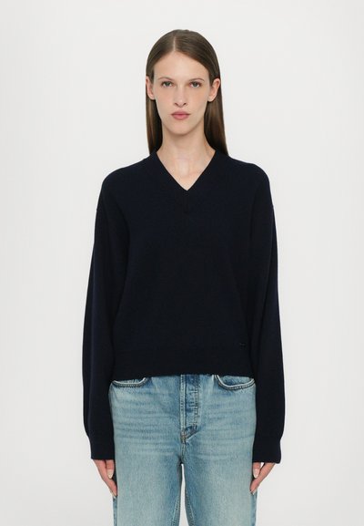 Pullover a V in maglia di colore blu navy, con maniche lunghe, vestibilità morbida, orlo a costine e un logo sottile accentato nella parte frontale vicino all'orlo.