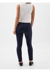 Pantalons ajustés bleu marine avec une texture lisse, présentant une taille mi-haute et deux poches arrière, associés à un haut sans manches blanc.