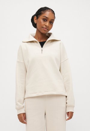 Beige zip-up sweatshirt med høj krave og afslappet pasform. Blødt stof og ribstrikkede manchetter. Parret med matchende lyse bukser.