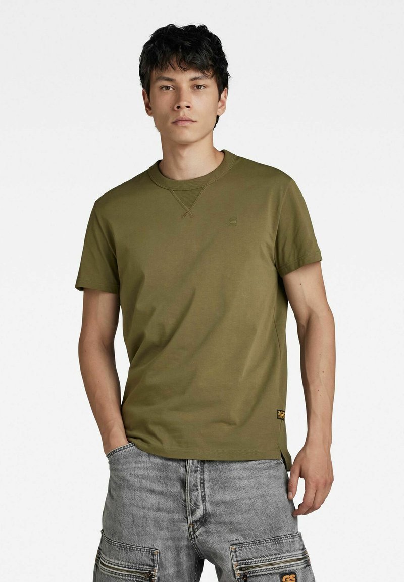 T-shirt in cotone verde oliva con maniche corte e scollatura a girocollo, caratterizzato da dettagli di cucitura discreti e un piccolo logo sul petto.