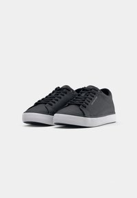 Baskets noires avec une texture lisse, un design à lacets, des semelles en caoutchouc blanches et un logo discret sur la languette et sur le côté.