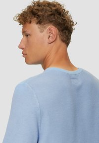 Hellblaues Kurzarmhemd mit strukturiertem Strickmuster, runder Halslinie und einem kleinen Akzent auf der Rückseite.