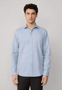 Camicia button-up azzurra chiaro realizzata in tessuto intrecciato, con maniche lunghe, colletto classico e una texture liscia. Motivo sottile visibile.
