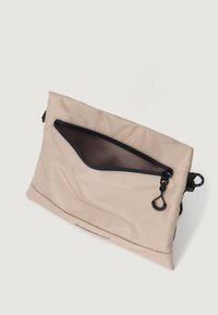 Bolso de mano de nylon beige con una superficie texturizada, cierre de cremallera negro y un clip. El interior presenta un color oscuro en contraste.