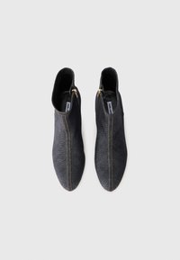 Botas de tornozelo em denim escuro com um formato elegante, apresentando fechos de correr dourados e costuras bege contrastantes ao longo das costuras laterais.