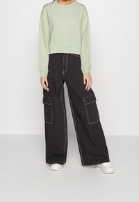 Felpa cropped verde menta con maniche lunghe, presenta cuciture decorative sulle spalle. Pantaloni cargo neri a gamba larga con multiple tasche.