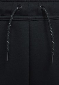 Pantalon de survêtement noir avec une texture douce, une ceinture élastique avec des œillets noirs et un cordon décoratif noir et blanc.
