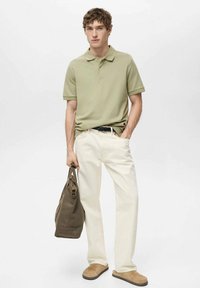 Polohemd aus weichem grünem Baumwollstoff, cremefarbene Hose, beige Slippers und eine braune Tragetasche mit strukturiertem Design und schlichten Akzenten.