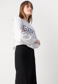 Grijze sweatshirt met het "GANT" logo in marineblauw, met brede mouwen. Draag over een lange, zwarte, strakke rok, wat een eenvoudige, strakke silhouet laat zien.