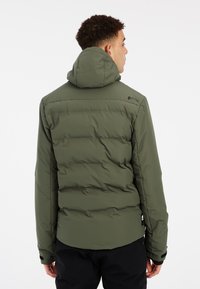 Chaqueta acolchada de color verde oliva con capucha, que presenta una textura suave, un detalle de logo en el hombro y puños elásticos. Acentos negros en el bajo.