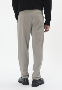 Gai pelēki bikses ar teksturētu audumu, kurām ir divas aizmugurējās kabatas un brīva piegriezuma, apvienotas ar melniem ādas apaviem.