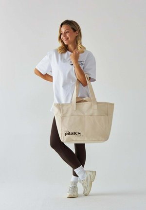 Beżowa torba Canvas z nadrukiem "to już czas na pilates" w kolorze czarnym. Posiada mocne uchwyty, prostokątny kształt i przestronne wnętrze.