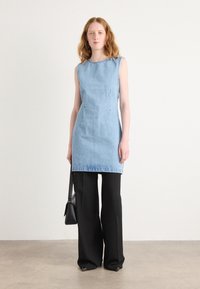 Τζιν αμάνικο φόρεμα σε ανοιχτό μπλε χρώμα, με πλαϊνές τσέπες και ίσια γραμμή, συνδυασμένο με μαύρο παντελόνι ψηλής μέσης και μικρή μαύρη τσάντα.