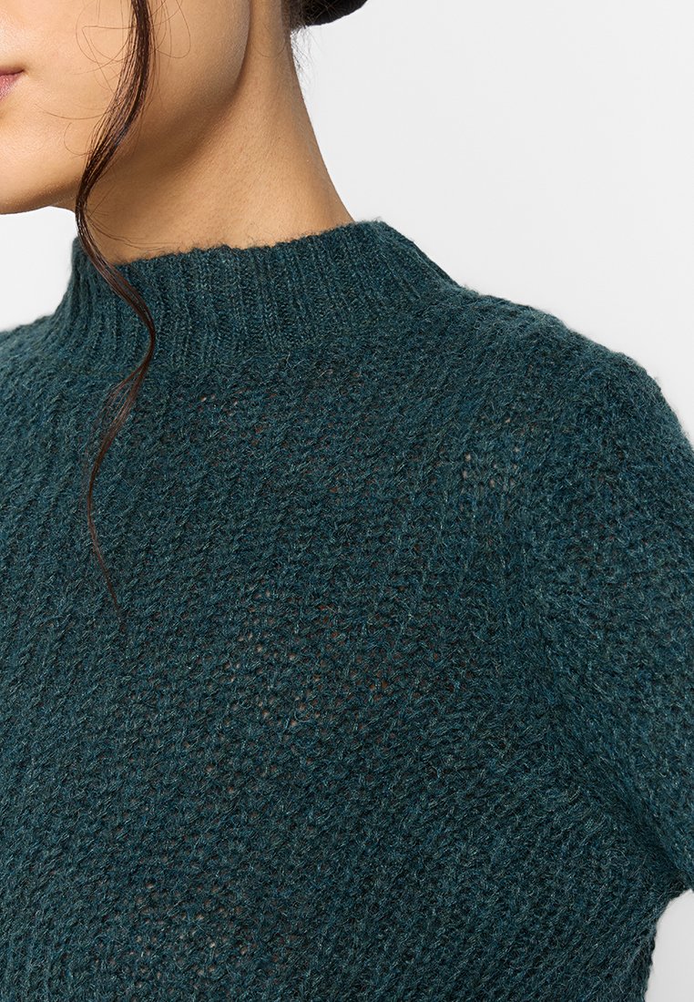Suéter de punto en azul profundo, con cuello alto, patrón texturizado y un corte holgado y relajado. Material suave con una profundidad sutil.