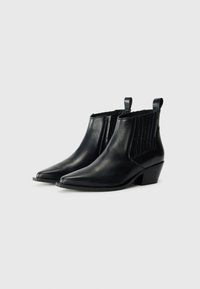 Botas de tobillo de cuero negro con punteras puntiagudas, paneles laterales elásticos y un tacón bajo en forma de cuña. Cuenta con acentos texturizados en los laterales.