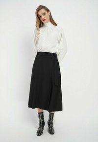 Biała bluzka w kropki z wysokim kołnierzem i długimi rękawami, w połączeniu z czarną spódnicą do kolan. Czarne botki za kostkę z przeszyciami.