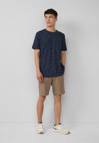 Marineblauwe gestructureerde t-shirt, korte mouwen, gecombineerd met lichtbeige shorts, witte sneakers met zwarte accenten, staand tegen een effen achtergrond.