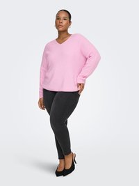 Light pink, v-neck knit sweater with long sleeves, paired with black slim-fit jeans and black high-heeled shoes. Simple, textured design.