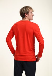 Långärmad skjorta i stark röd färg, tillverkad av mjukt tyg. Enkel design med rund halsringning och figurnära silhuett.