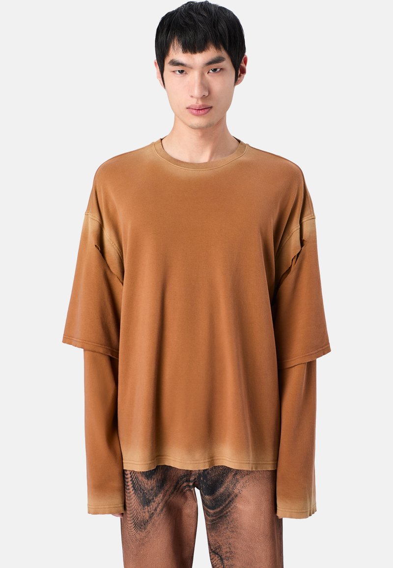 Oversized brauner Sweatshirt mit Rundhalsausschnitt, das mit geschichteten kurzen Ärmeln und einer glatten Textur ausgestattet ist, kombiniert mit gemusterten braunen Hosen.