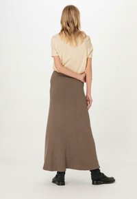 Beige T-Shirt, kombiniert mit einem langen, gerippten, braunen Strickrock. Der Rock hat eine enganliegende Taille und eine fließende Silhouette, die durch schwarze Schuhe ergänzt wird.