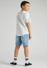 Biała bawełniana koszulka, jasnoniebieskie dżinsowe szorty, czarne trampki i białe skarpetki w czarne paski. Chłopiec odwrócony plecami do kamery.