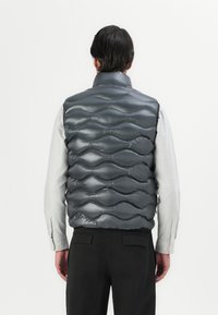 Gray puffy vest with a wave-patterned design, made from a shiny material. It has a high collar and is paired with a striped shirt.