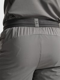 Close-up van een persoon die grijze sportshorts draagt en een bijpassend topje met een zwarte elastische tailleband met twee naar beneden wijzende pijlen.