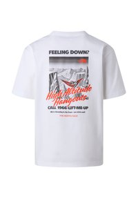 Bílé tričko s potiskem na zádech, na kterém je osoba v hamace mezi skalami, s pozadím hor a textem propagujícím "Vysoce položené odpočinky."