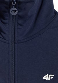 Sweat à capuche zippé bleu marine avec col montant, tirant de fermeture éclair visible marqué "4F" et logo blanc "4F" sur la poitrine.